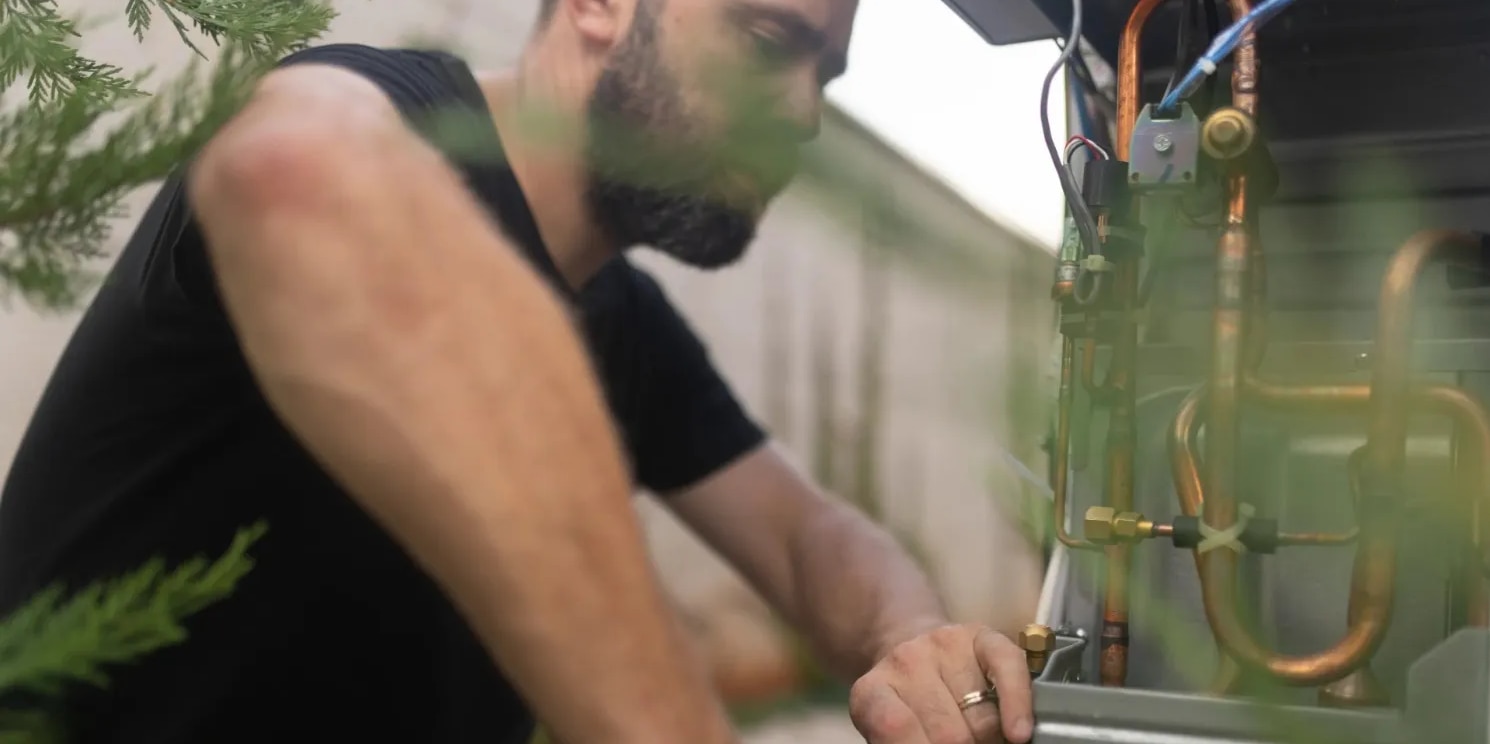 Technician servicing an outdoor heat pump unit with copper refrigerant lines